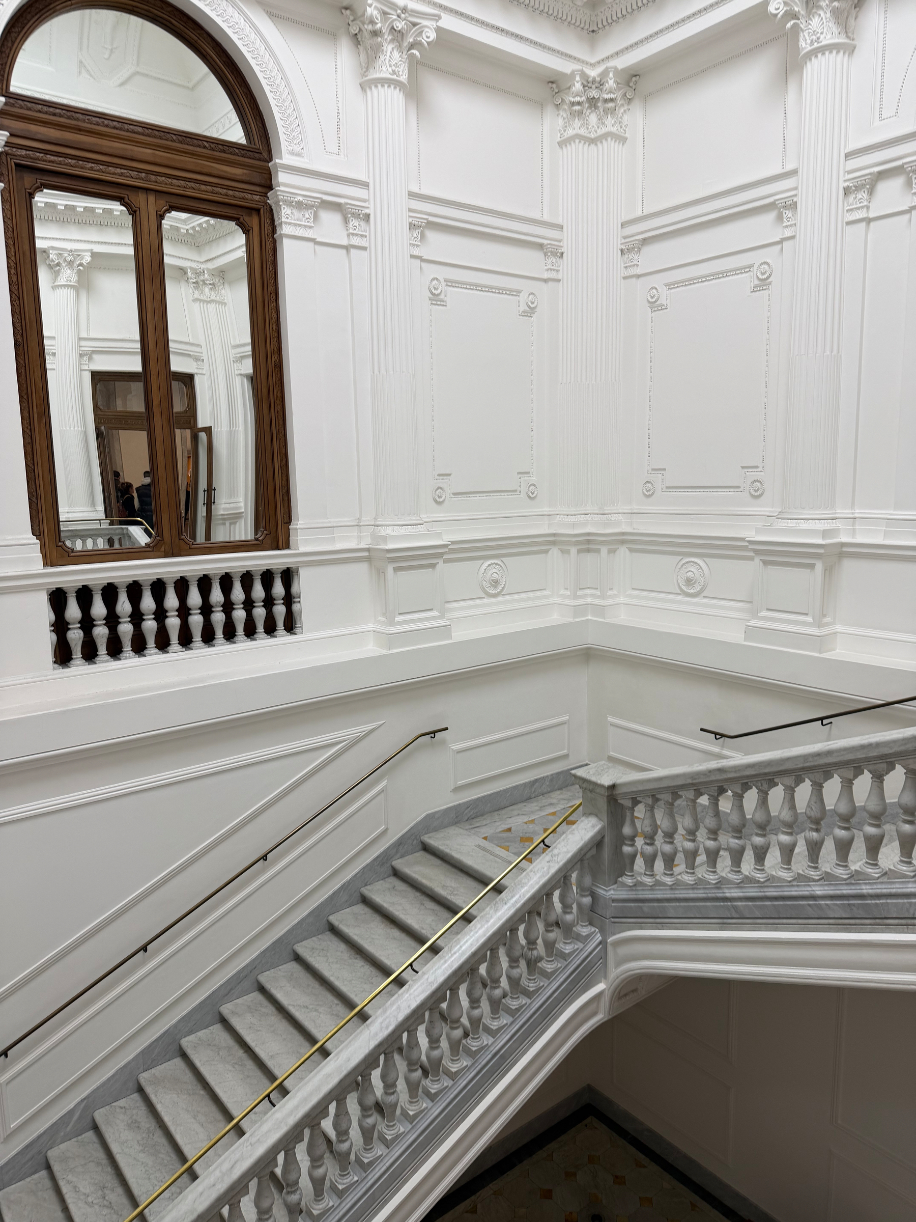 Auto-generated description: A grand, white interior features an ornate staircase with a marble handrail and decorative molding.